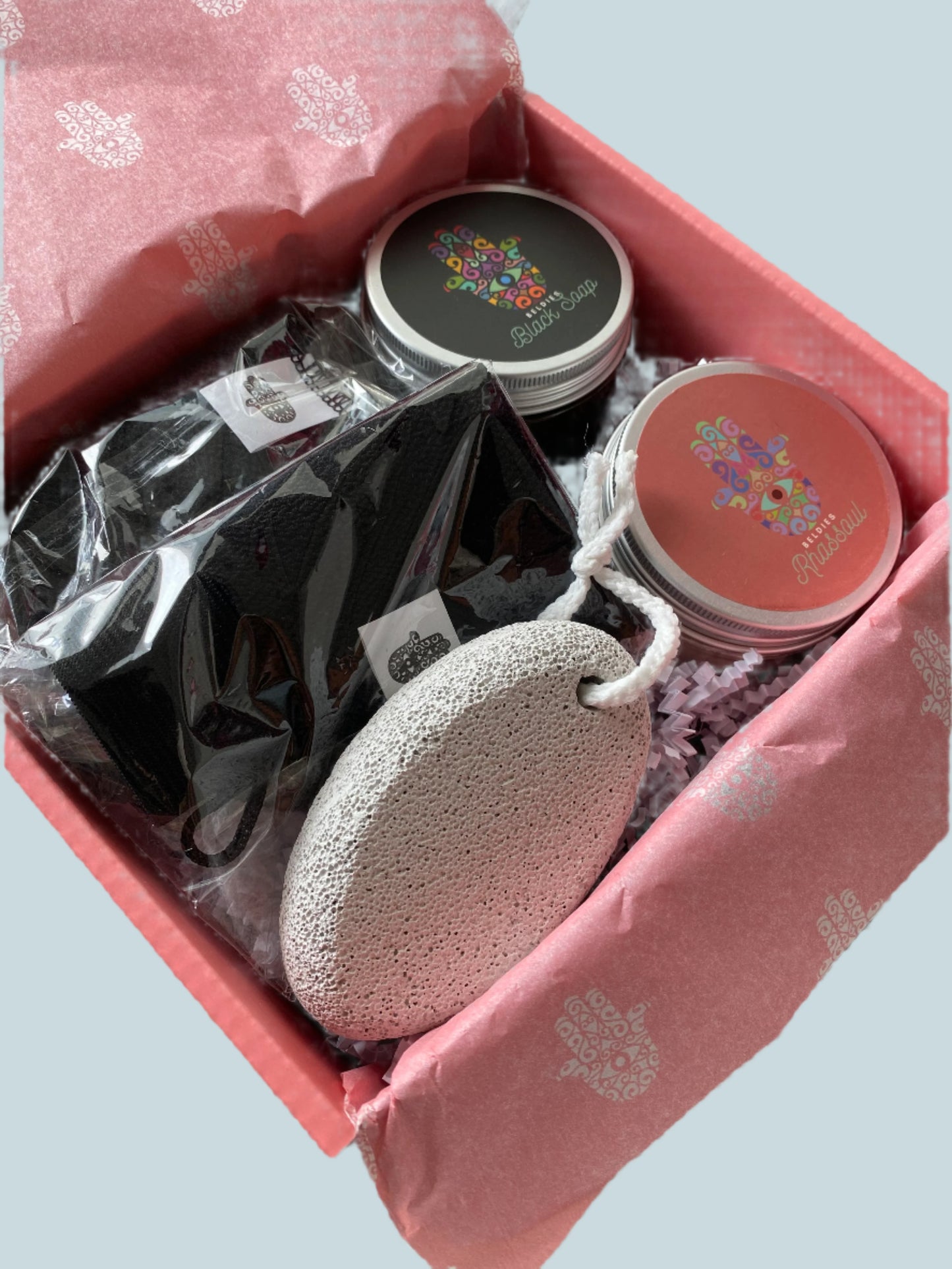 Close-up image of Beldies hammam kit, including black soap, rhassoul clay, exfoliating gloves aka kessa, and a pumice stone.
