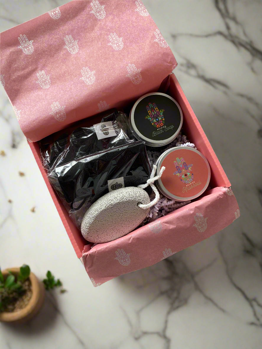 Close-up image of Beldies hammam kit, including black soap, rhassoul clay, exfoliating gloves aka kessa, and a pumice stone.